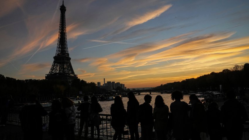 People watch the skyline as the cross the Debilly bridge near the Eiffel Tower during sunset in Paris, Saturday, Nov. 12, 2022.