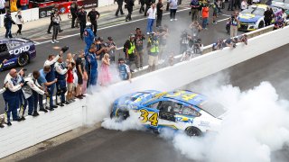 Michael McDowell, driver of the No. 34 Horizon Hobby Ford, celebrates with a burnout in front of his crew and family after winning the NASCAR Cup Series Verizon 200 at the Brickyard at Indianapolis Motor Speedway on Aug. 13, 2023 in Indianapolis.