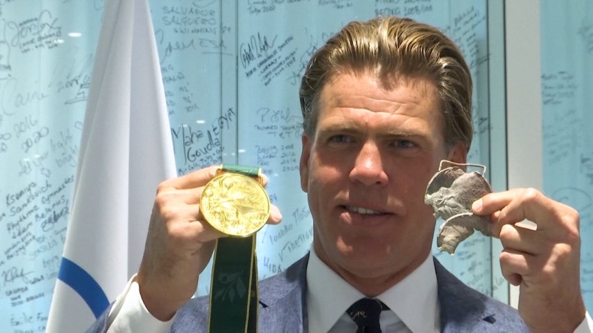 Gary Hall Jr. holds up a new medal and a burnt one