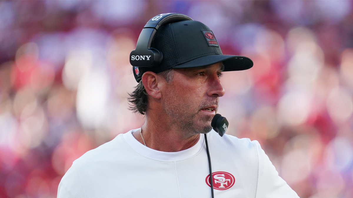 Jerry Rice speaking at a Super Bowl event podium, gesturing emphatically while discussing NFL strategies with a microphone in hand.